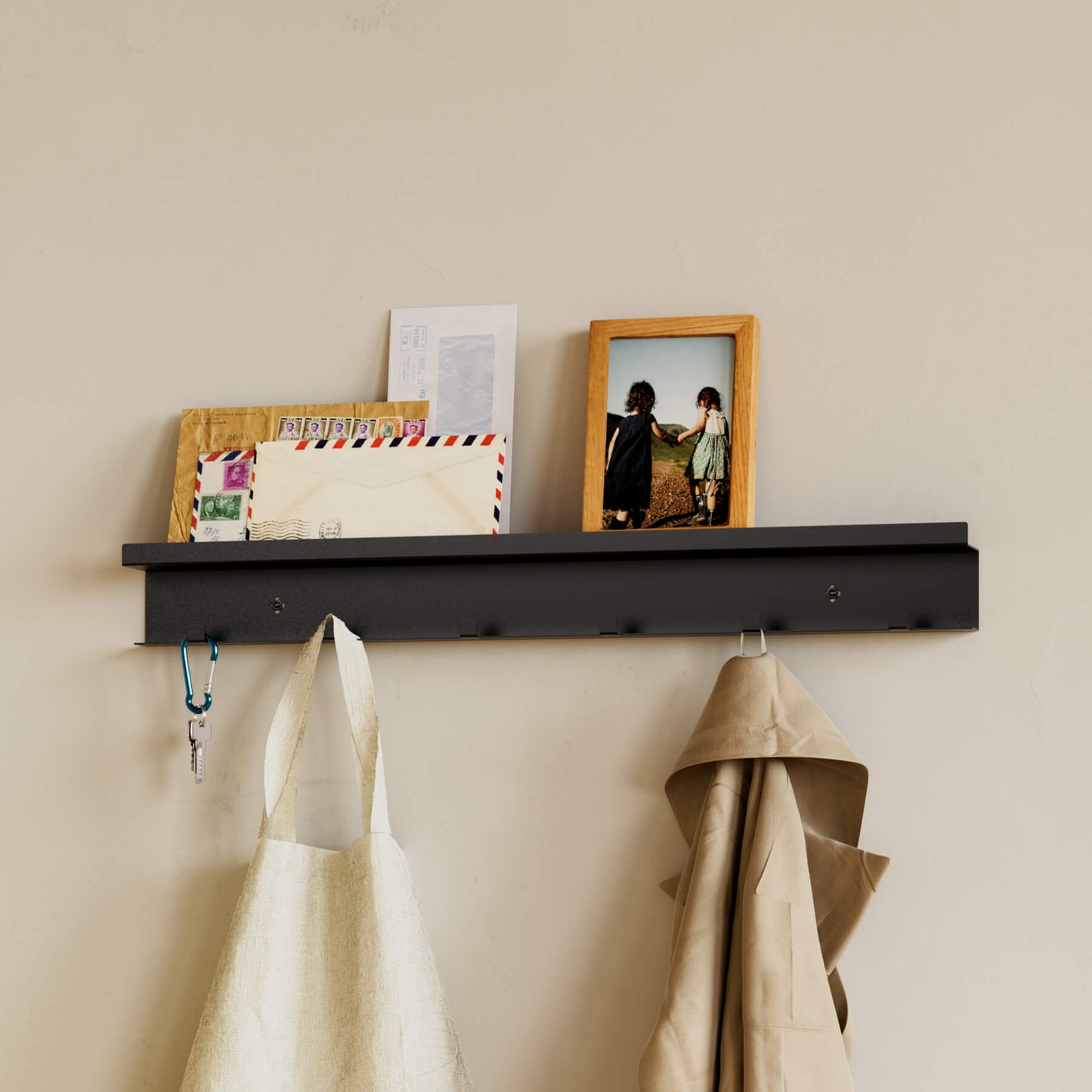 Schwarze Garderobe Commeo montiert an der Wand besetzt mit einer Jacke, einem Beutel, Post und einem Bilderrahmen aus Holz.