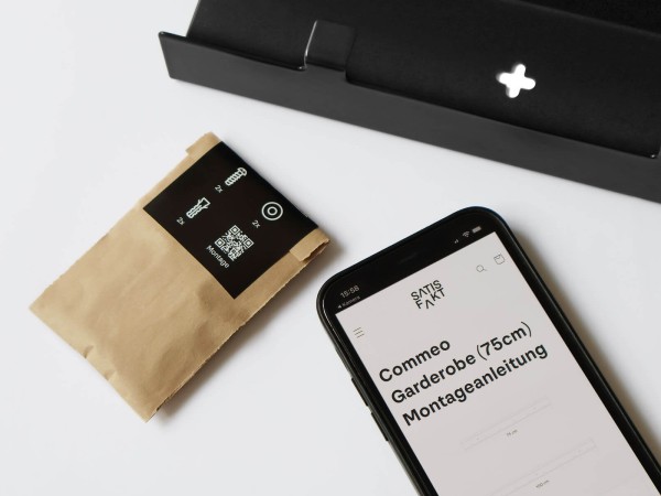 Montagematerial in einer Papiert&uuml;te neben einem Smartphone mit der digitalen Montageanleitung f&uuml;r die Garderobe Commeo